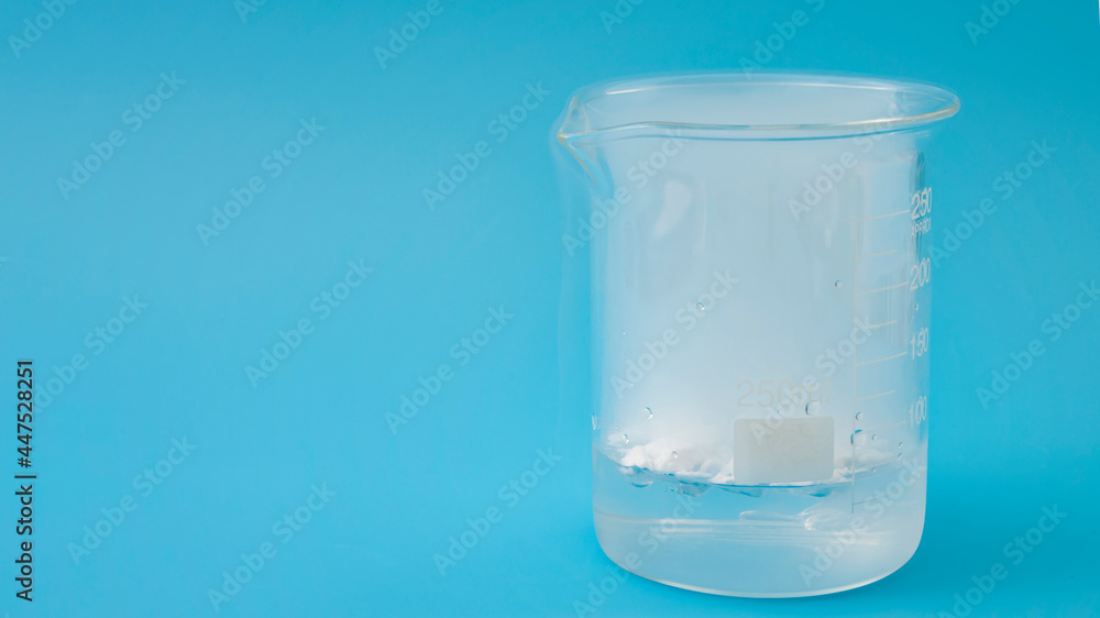 Science laboratory, scientific experiment and lab test concept with dry ice in a glass chemistry beaker isolated on blue background with copy space Science laboratory, scientific experiment and lab test concept with dry ice in a glass chemistry beaker isolated on blue background with copy space