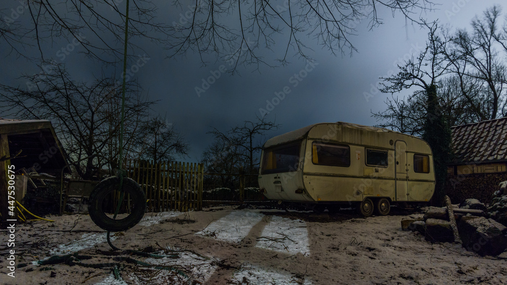 Old camping trailer standing at a farm at night in winter, Germany