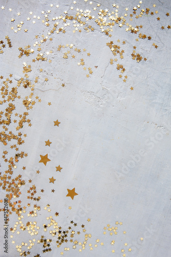 Golden glitter star shaped confetti. Top view, close up, on light gray concrete background