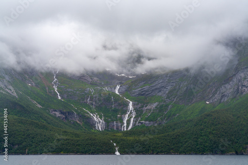 waterfalls drop down through lush green forest into a Norwegian fjord on the Helgeland Coast photo