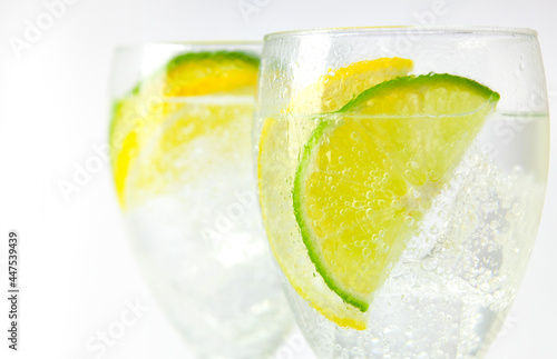 Two stemmed glasses with sparkling ice water and lemon and lime slices on white