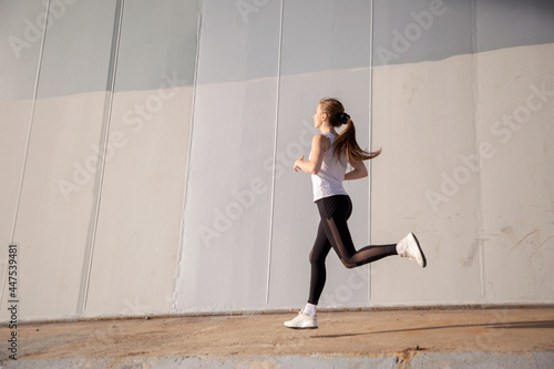 A young woman in a white T-shirt and black pants runs under the bridge in the evening. Running trainings in the city. Preparing for the competition.