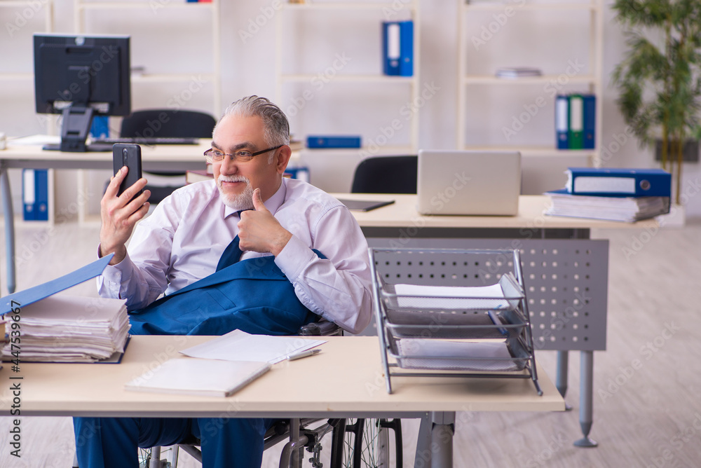 Old male employee in wheel-chair sitting in the office Old male employee in wheel-chair sitting in the office
