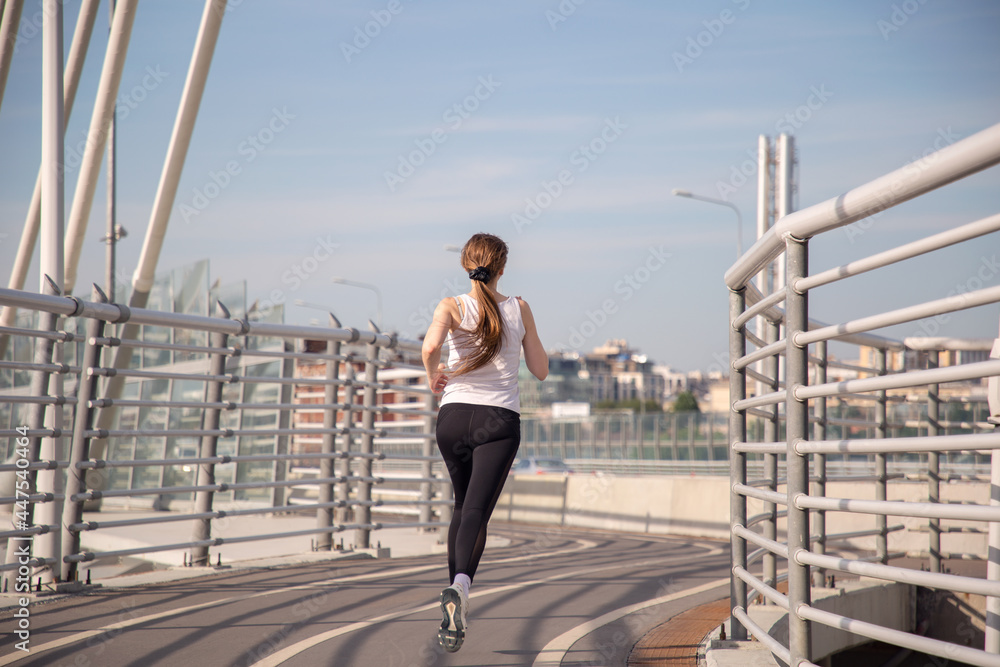 A girl athlete runs on a treadmill across the bridge. Evening running training in the city. Preparing for the competition. Sports ammunition. Betancourt Bridge in St. Petersburg.
