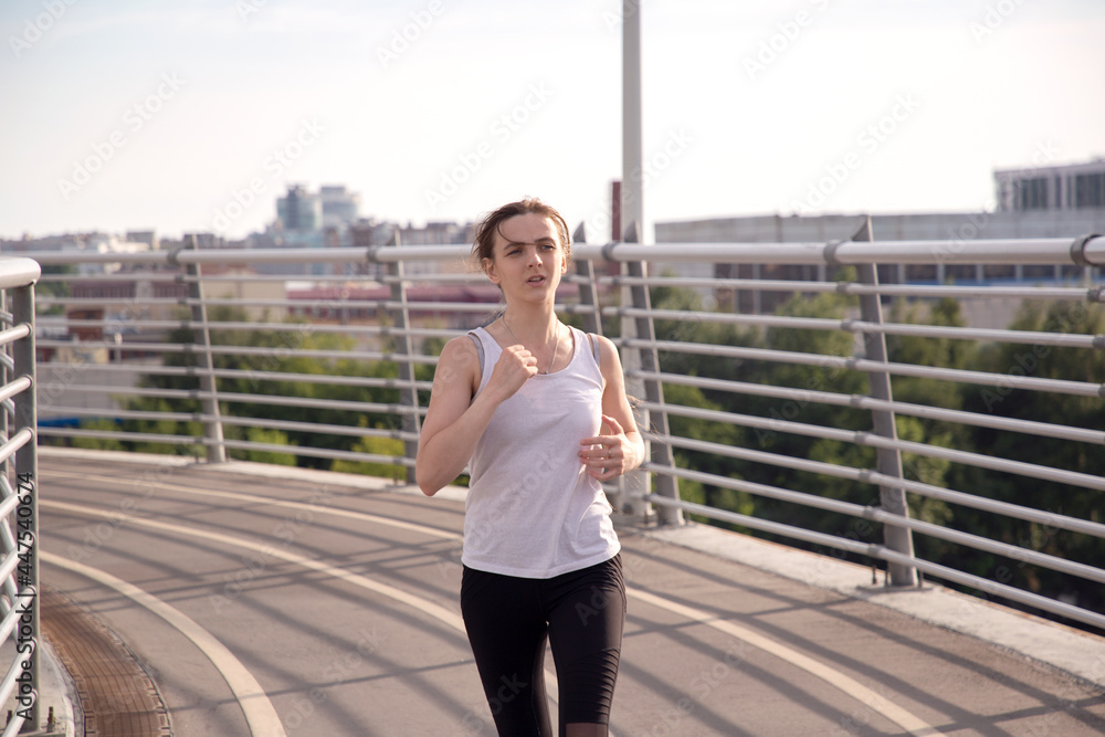 A girl athlete runs on a treadmill across the bridge. Evening running training in the city. Preparing for the competition. Sports ammunition. Betancourt Bridge in St. Petersburg. A girl athlete runs on a treadmill across the bridge. Evening running training in the city. Preparing for the competition. Sports ammunition. Betancourt Bridge in St. Petersburg.