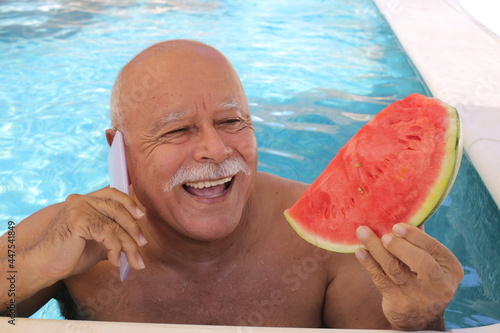 Senior man calling from swimming pool while eating watermelon