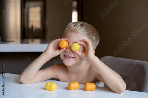 A little boy blonde plays with yellow capsules from kinder surprise, smiles, he is happy.