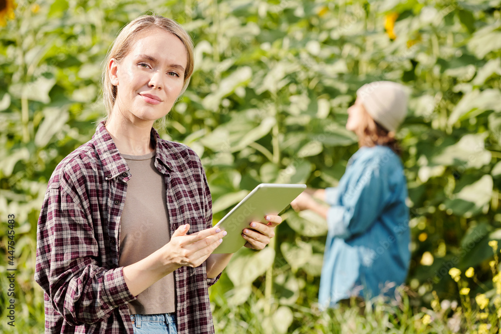 Mature female farmer in workwear standing in front of camera and using touchpad