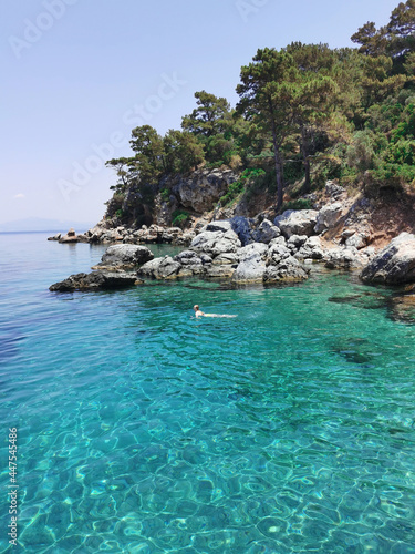 Young girl in bikini swims on the azure beach with rocks and pine trees. The Aegean sea. Turkey, Kusadasi.