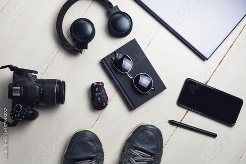 Modern lifestyle objects. A headphone, laptop smartphone, keys, sunglasses, journal, camera and shoes on a wooden background. Flat lay.