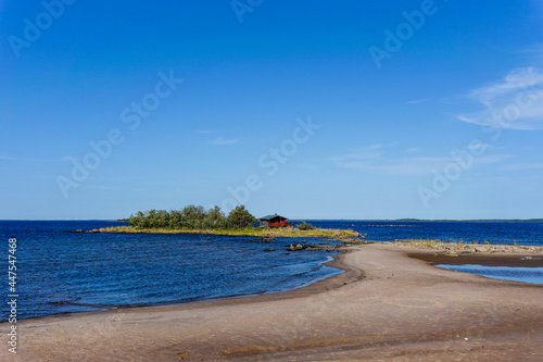 Fototapeta Naklejka Na Ścianę i Meble -  picturesque coastal landscape on the Baltic Sea with a small red cottage on an island behind a sandy beach under a blue sky