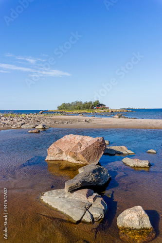picturesque coastal landscape on the Baltic Sea with a small red cottage on an island behind a sandy beach under a blue sky
