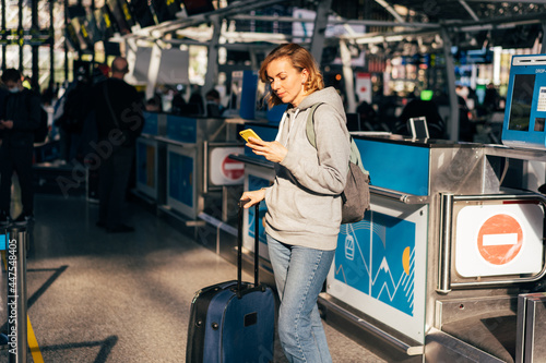 A young woman stands at the airport with a mobile phone and luggage and waits for check-in.