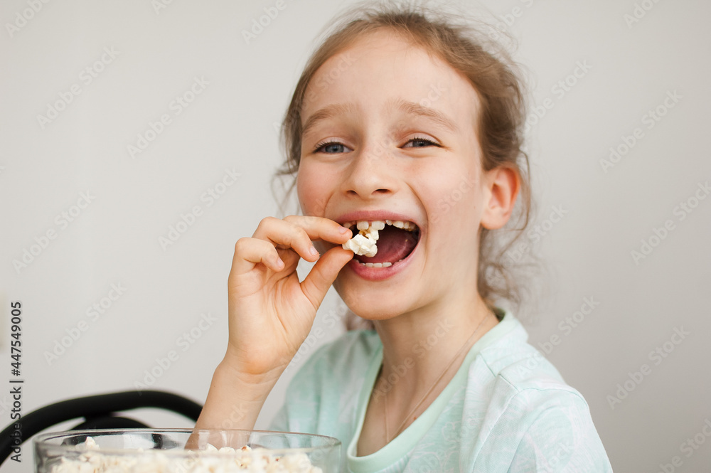 Portrait of a funny and excited schoolgirl girl on a white background, smiling and eating popcorn from a bowl Portrait of a funny and excited schoolgirl girl on a white background, smiling and eating popcorn from a bowl