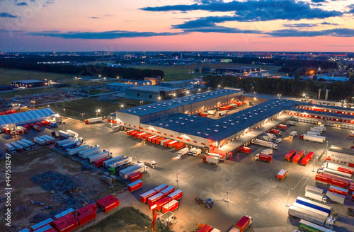Aerial view of a logistics park with a  loading hub. A lot of semi-trailer trucks standing at warehouse ramps for loading and unloading goods at dusk