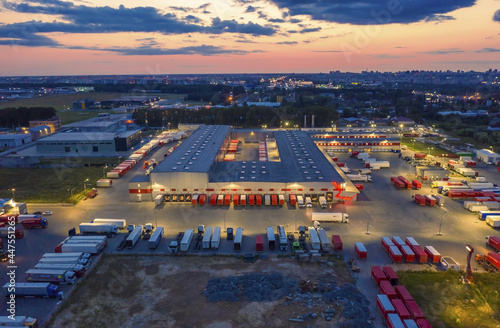 Aerial view of a logistics park with a  loading hub. A lot of semi-trailer trucks standing at warehouse ramps for loading and unloading goods at dusk