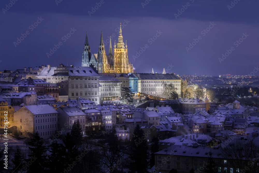 Prague Castle in Hradcany district  with an illuminated street below at night in winter covered with snow captured from Petrin Hill