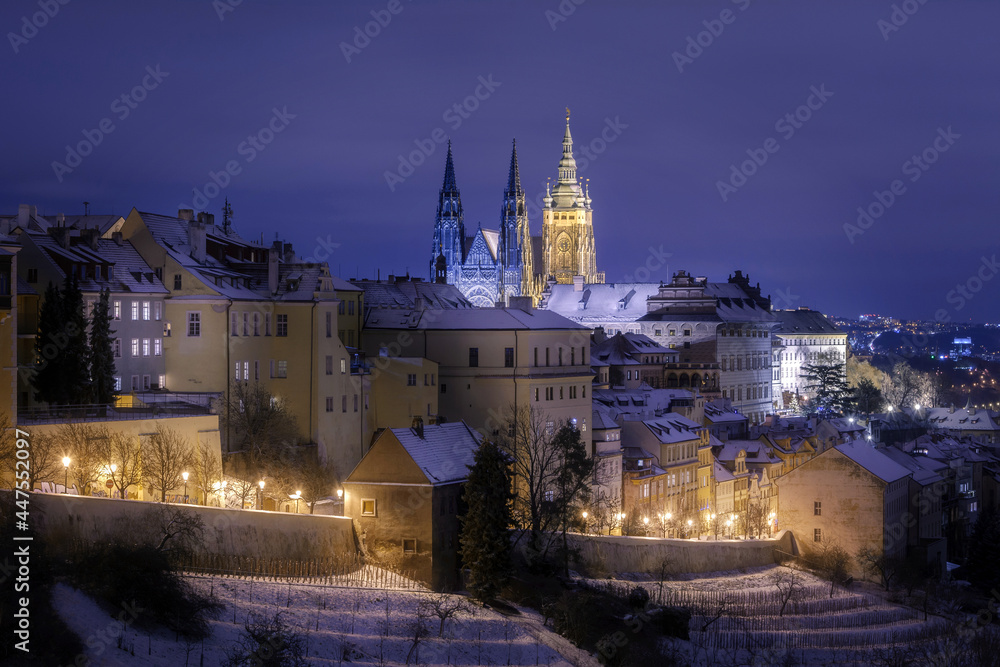 Prague Castle in Hradcany district  with an illuminated street below at night in winter covered with snow captured from Petrin Hill