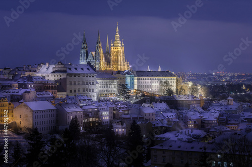 Prague Castle in Hradcany district with an illuminated street below at night in winter covered with snow captured from Petrin Hill