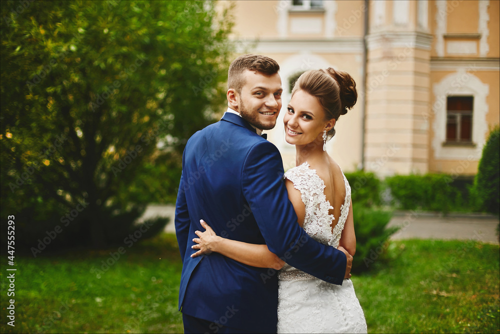 A happy couple of newlyweds hugging after the outdoor wedding ceremony. Beautiful model girl in a wedding dress and handsome man in trendy blue suit