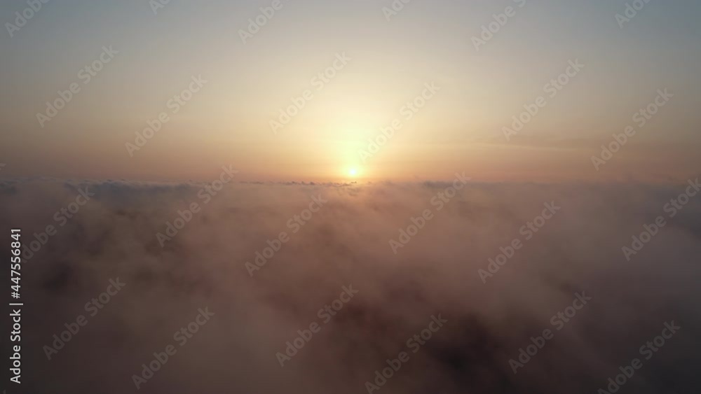 Sun is hidden behind the clouds at sunset the fog. Moving white clouds blue sky scenic aerial view. Drone flies high back in blue sky through the fluffy clouds in the evening at the bright sun Sun is hidden behind the clouds at sunset the fog. Moving white clouds blue sky scenic aerial view. Drone flies high back in blue sky through the fluffy clouds in the evening at the bright sun