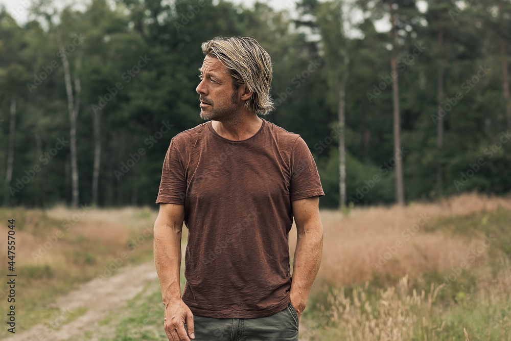 Blonde man with a stubble beard in a brown t-shirt on a sandy pa