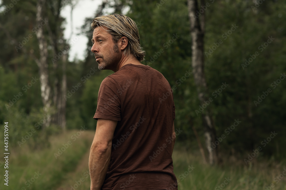Naklejka premium Blonde man with a stubble beard in a brown t-shirt looks over hi