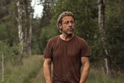Blonde man with a stubble beard in a brown t-shirt on a forest p