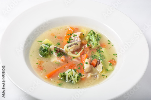 Light fish soup with vegetables and broccoli in white plate.