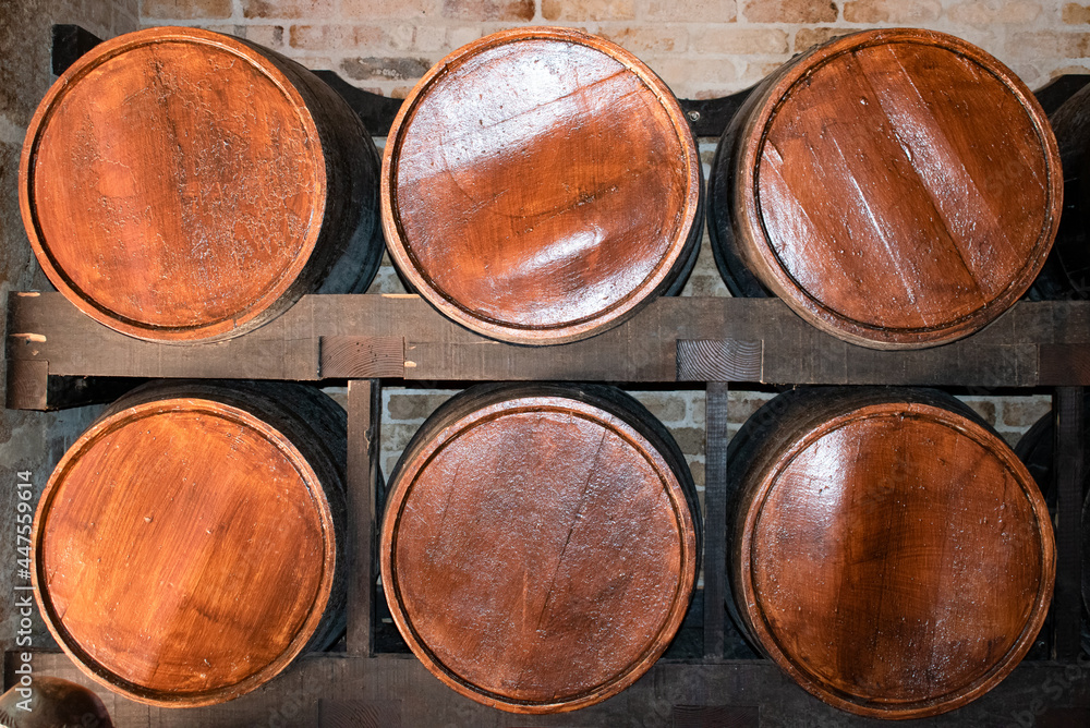 Six wooden alcohol barrels on a shelf in a room. These vintage containers can store wine, rum, beer, whisky, brandy, tequila and other alcoholic beverages.