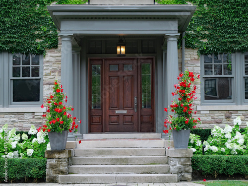 House with elegant wood grain door, surrounded by ivy and red amaryllis and white hydrangea flowers