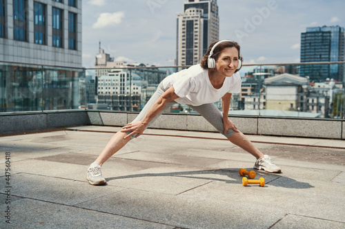 Smiling pretty aged woman exercising on urban roof
