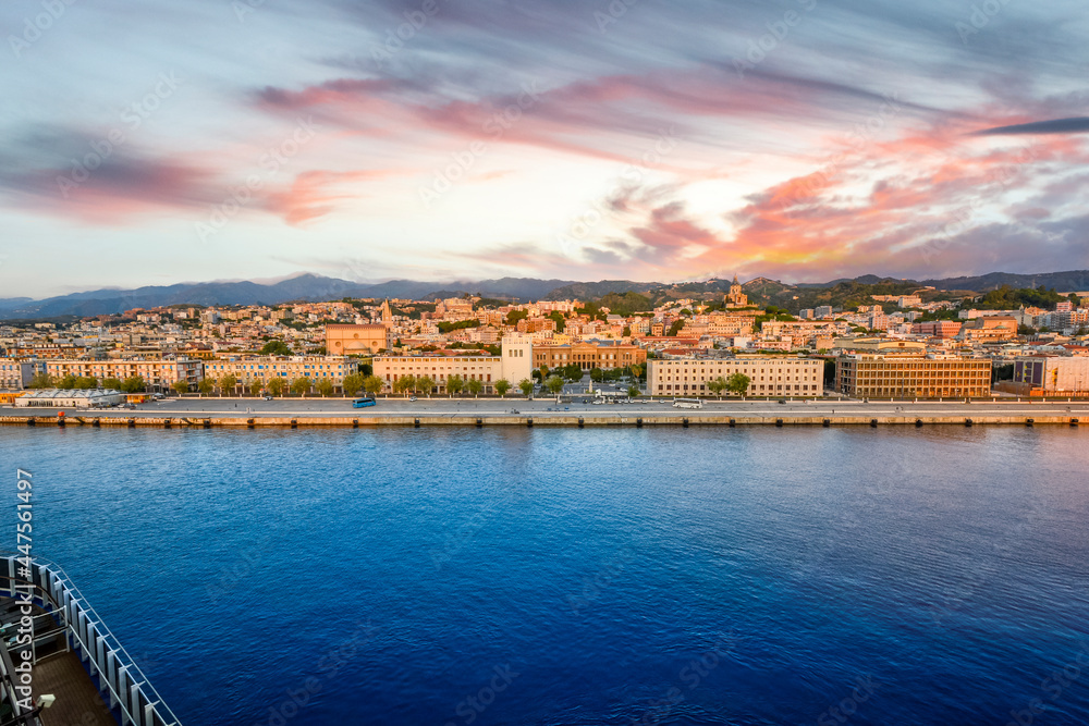 View from a cruise ship of the port and skyline of Messina on the island of Sicily, the main tourist hub for cruise lines, under a colorful sky.