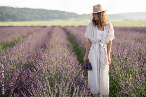 Young woman staying on lavender field with bouquet of violet flowers and enjoy the beauty of nature. Calmness and mindful concept. Copy space 