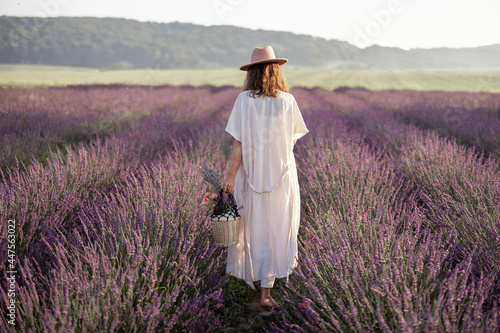Young woman staying back on lavender field with bouquet of flowers and enjoy the beauty of nature. Calmness and mindful concept. 