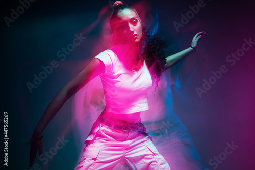 Colourful portrait of young mixed race girl dancing in studio. Long exposure. Colored neon light. © Georgii