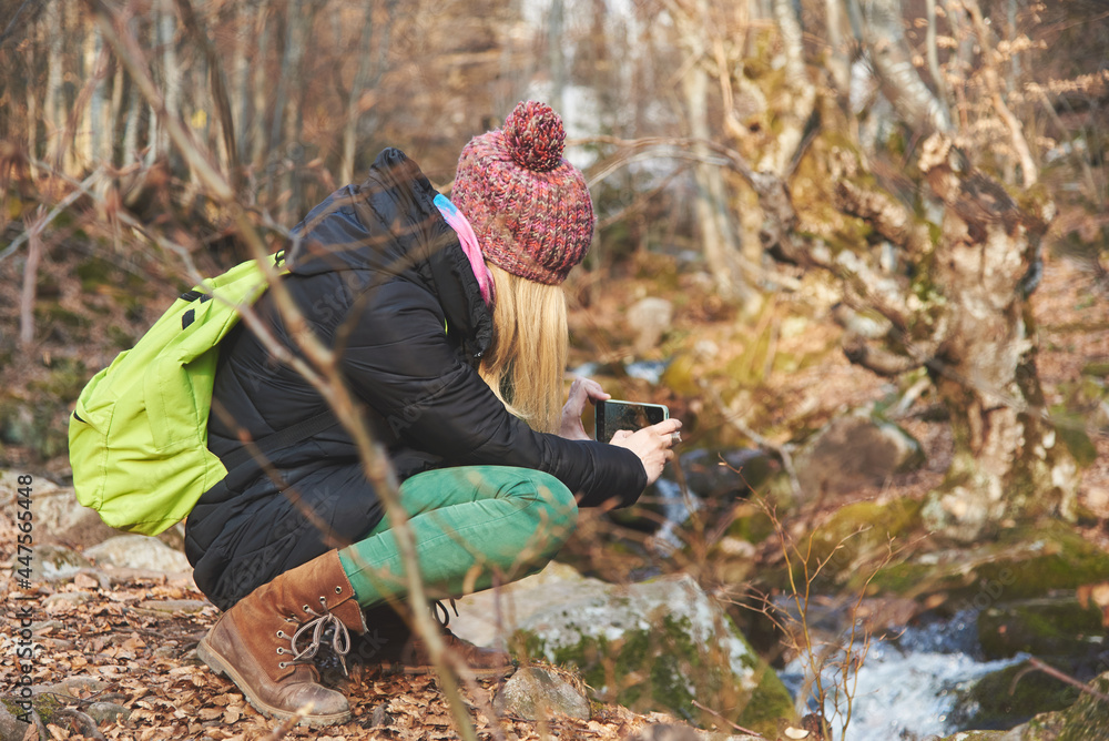 Young woman, a hiker or a backpacker, walking through the forest, taking images and photographs of winter nature, cold river and autumn leaves Young woman, a hiker or a backpacker, walking through the forest, taking images and photographs of winter nature, cold river and autumn leaves