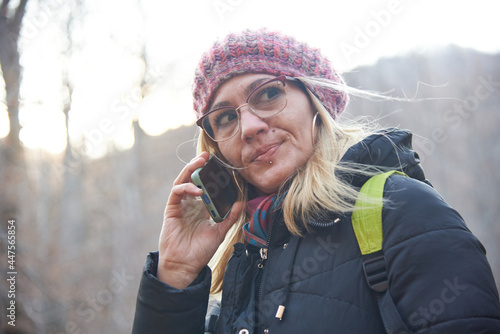Young blonde woman on a holiday, enjoying her time in autumn nature, talking on her cell phone, trying to navigate through the forest