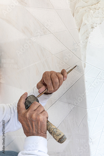Detail of artist's hands sculpting marble with hammer and chisel