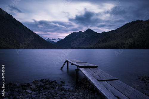 Long exposure evening mountain landscape. Old wooden pier on the lake. Mountain sunset and dramatic sky.