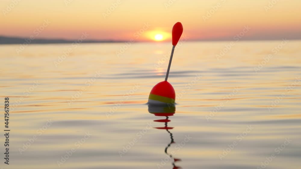 Fishing float sways on surface of sea water in early dawn light lens flares. Fishing. Path from sun on water. Hobby. Relax. Lifestyle