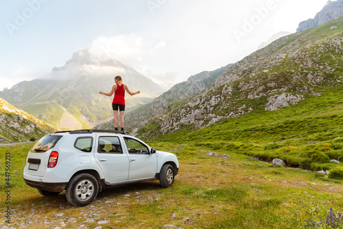 Fototapeta Naklejka Na Ścianę i Meble -  young girl with arms raised and on the roof of his off-road car watching the mountain after a day of travel and adventure. Active tourism. mountain activities.