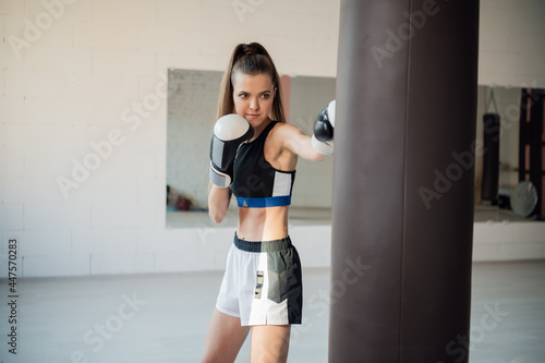 Beautiful kickboxing woman training punching bag in fitness studio. © romankosolapov