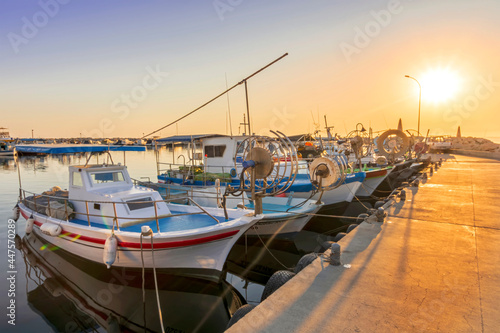 tranquil sunrise in fishing docks with sunny pier , leading far to sea and golden sun with sailing boats moored around
