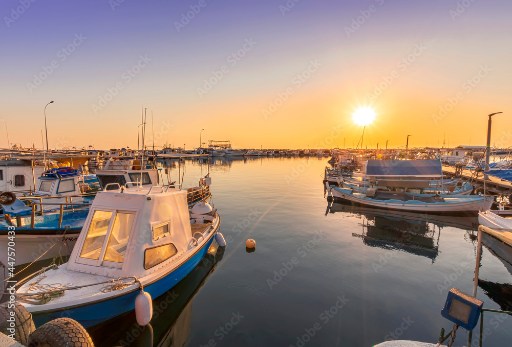 tranquil sunrise in fishing docks at a small port with calm sea and golden sun , old sailing boats moored around marina
