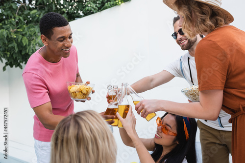 excited multiethnic friends clinking bottles of beer during summer party