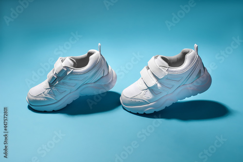 two white child flying in the air sneakers simulate walking isolated on a blue background.