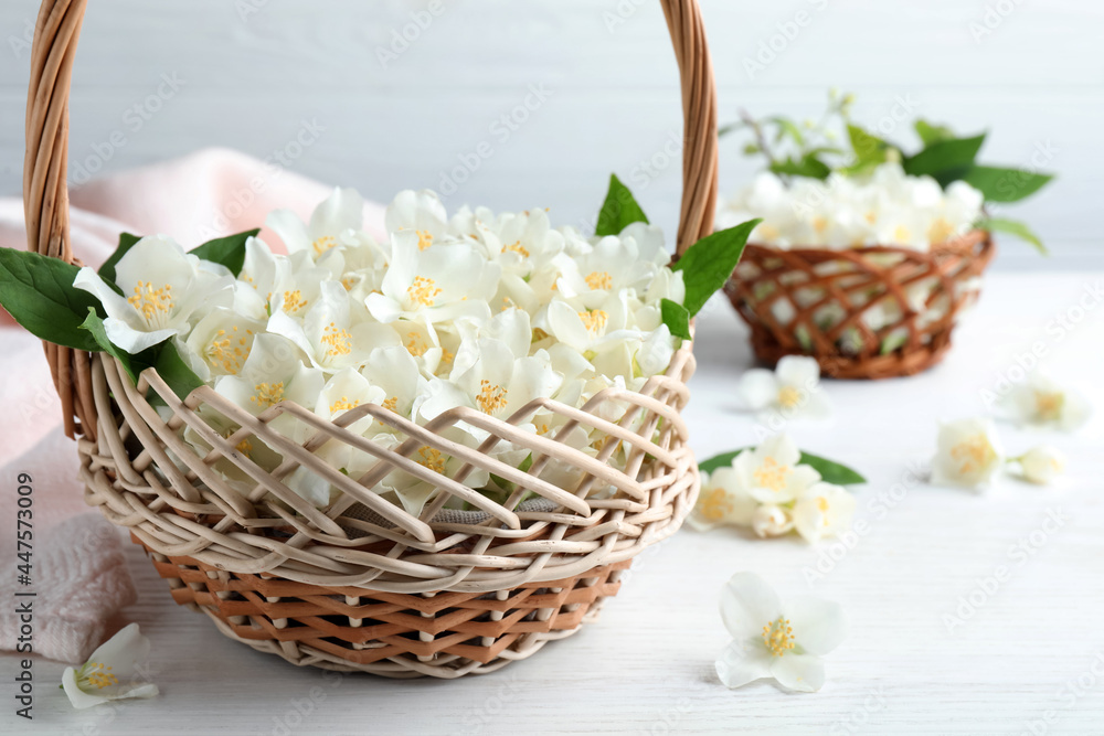 Beautiful jasmine flowers in wicker basket on white wooden table
