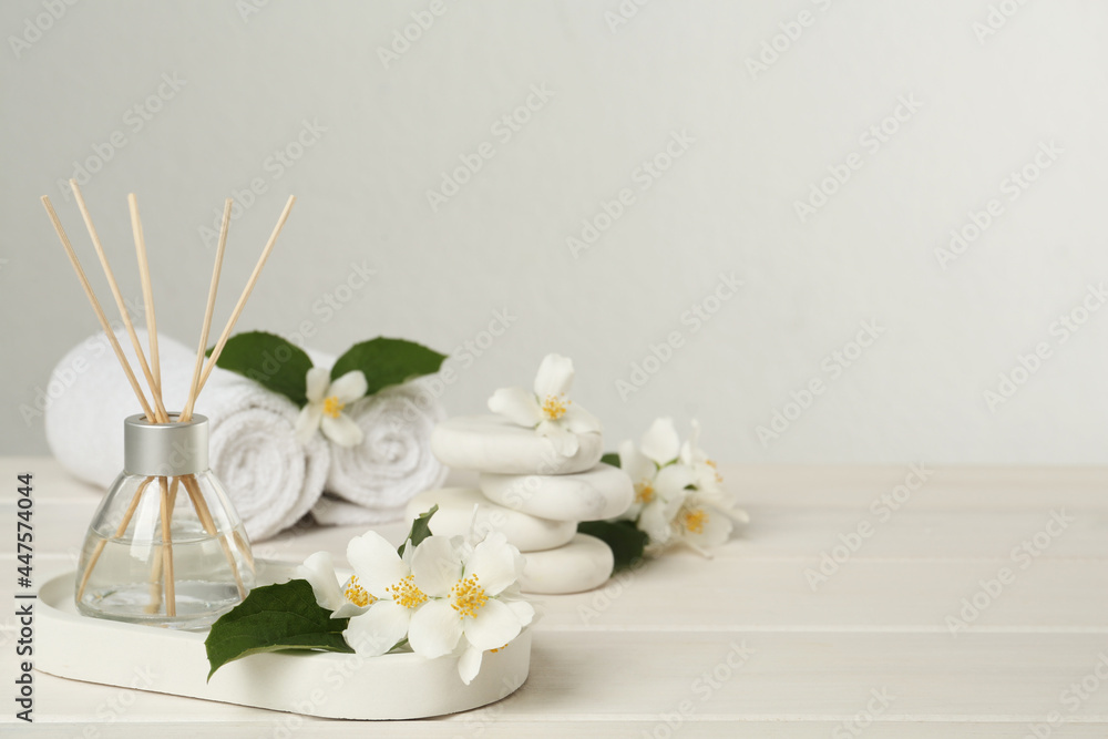 Air reed freshener and beautiful jasmine flowers on white wooden table, space for text