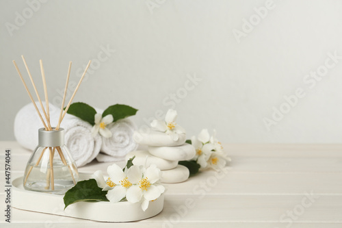Air reed freshener and beautiful jasmine flowers on white wooden table  space for text